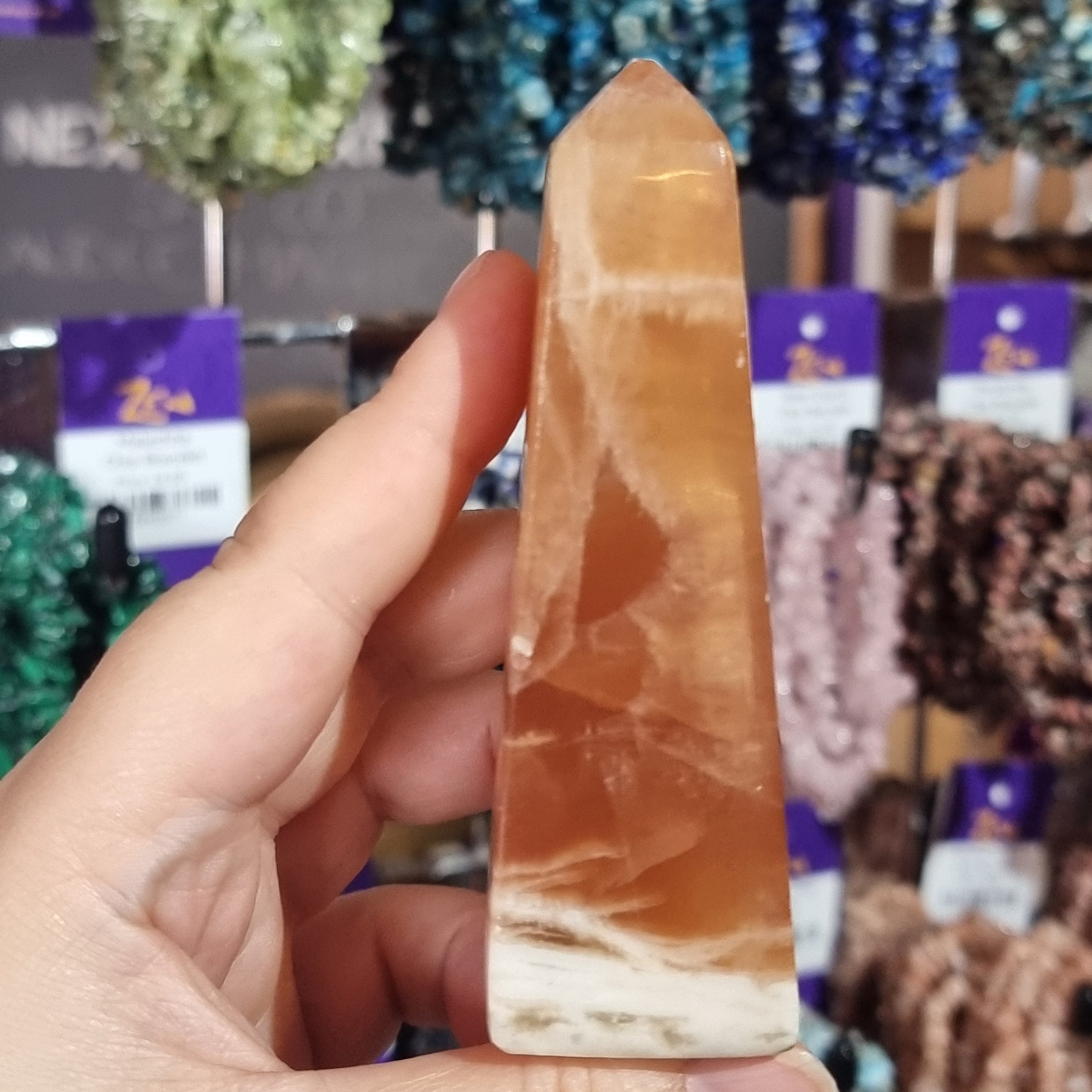 Hand holding a polished orange stone with blurred gemstone display in the background