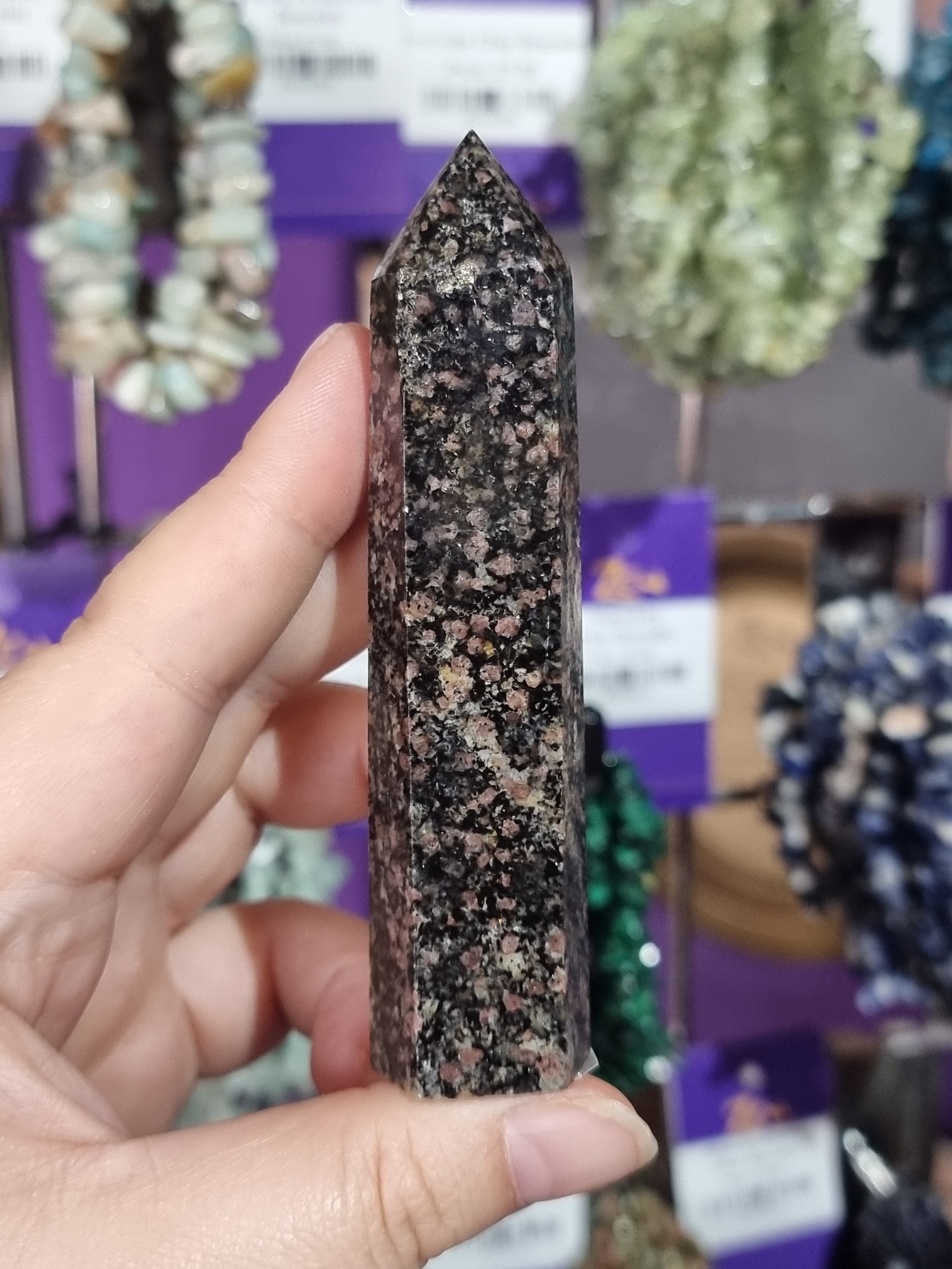 Hand holding a speckled stone tool with blurred gemstones in the background