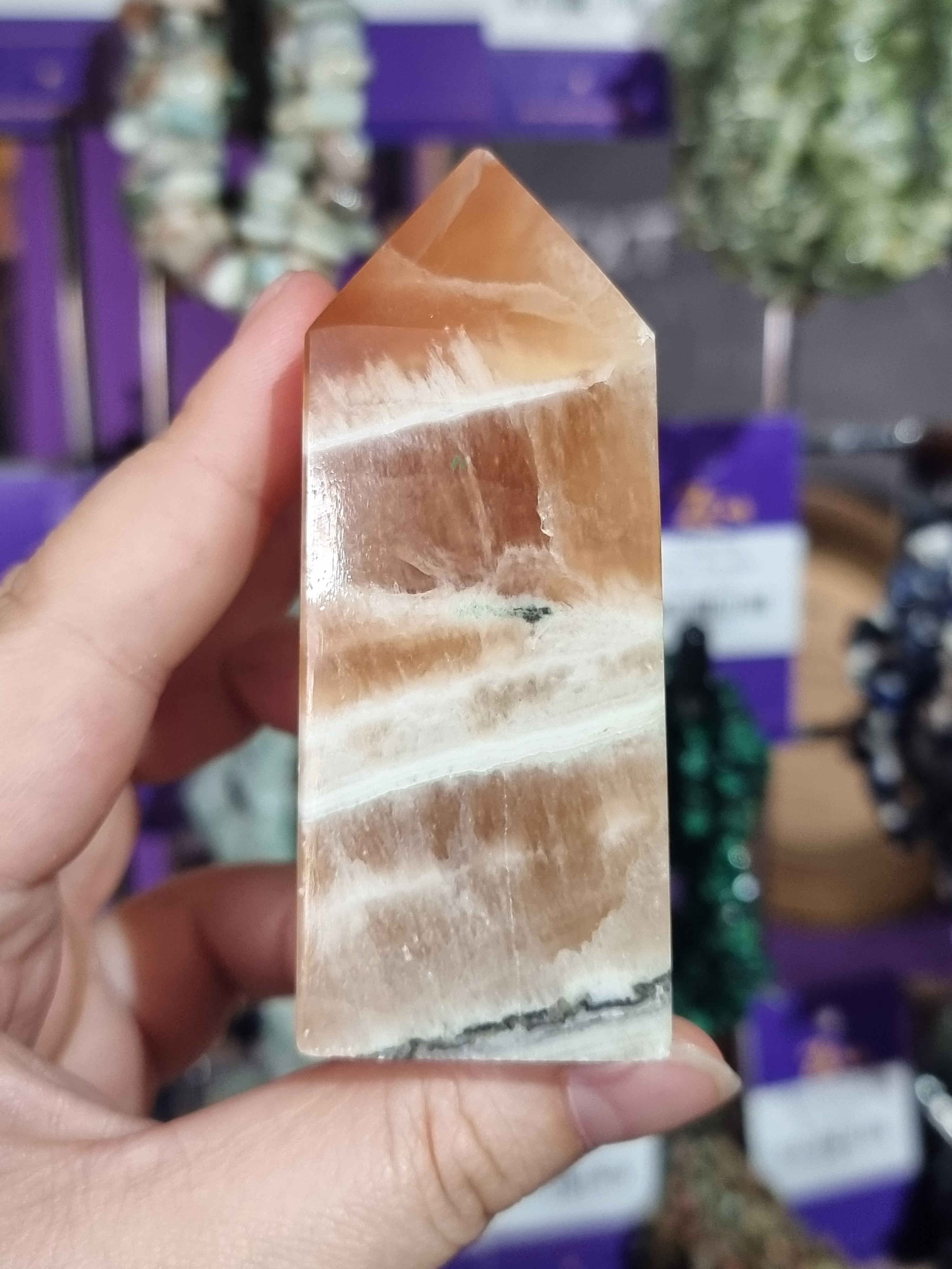 Hand holding a crystal with a blurred background of shelves with various items.