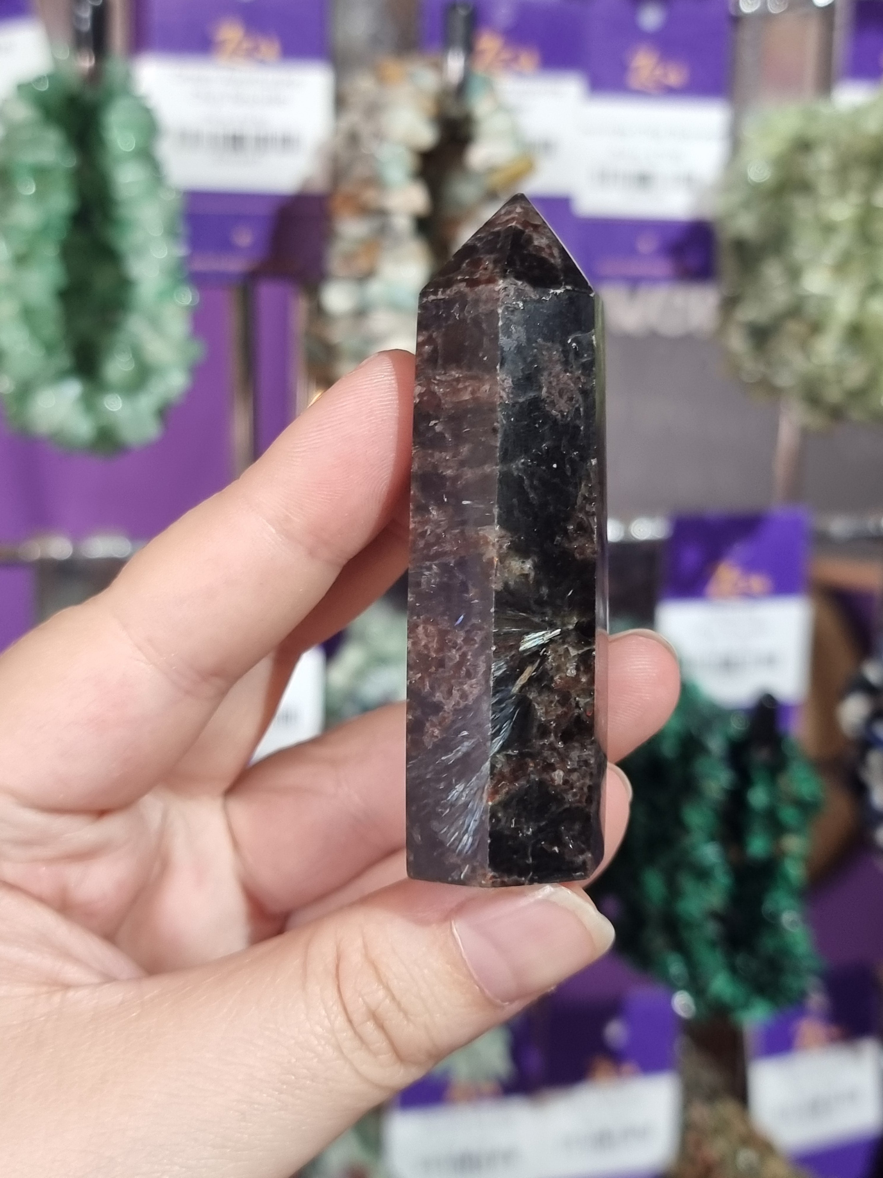 Hand holding a polished crystal against a blurred background with similar crystals.