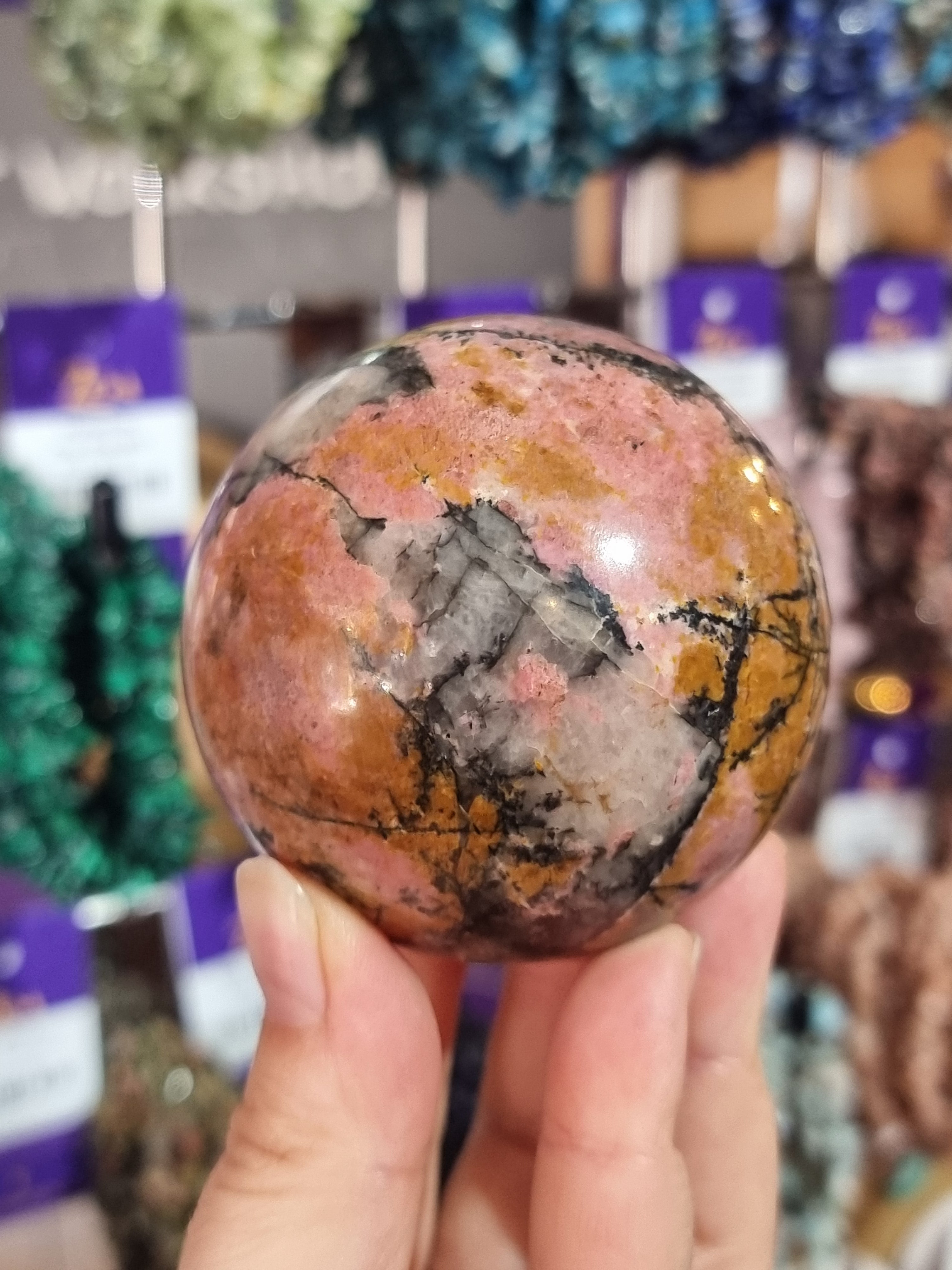 Hand holding a large rhodonite crystal ball with a blurred store background